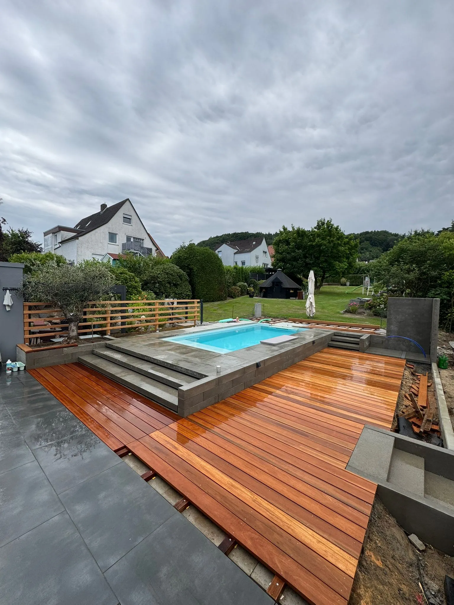 Poolgarten von oben: Deck an der Terrasse. Der Belag wächst aus der Terrasse heraus bis ans Wasser.