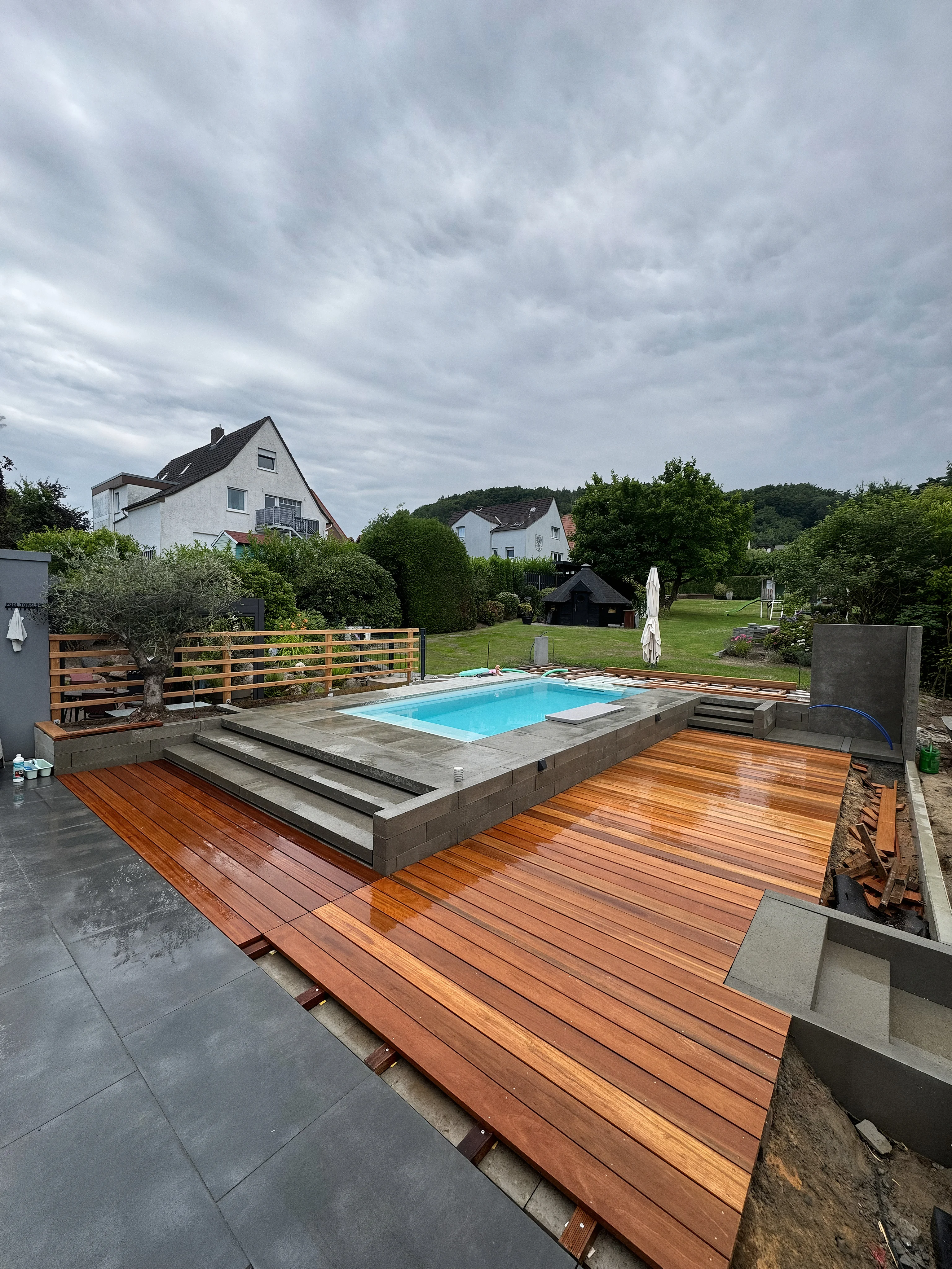 Der fertige Poolgarten bei Tag: frisches Holzdeck, Becken, Sichtschutz.