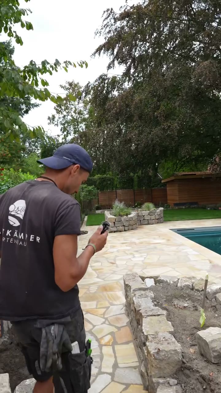 Ein Teammitglied steht vor einer Natursteinmauer neben dem Pool und erklärt den Baustand.